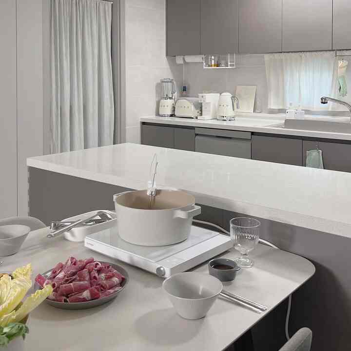 Modern kitchen in white and gray tones featuring a dining table with cooking pot and ingredients, creating a clean atmosphere