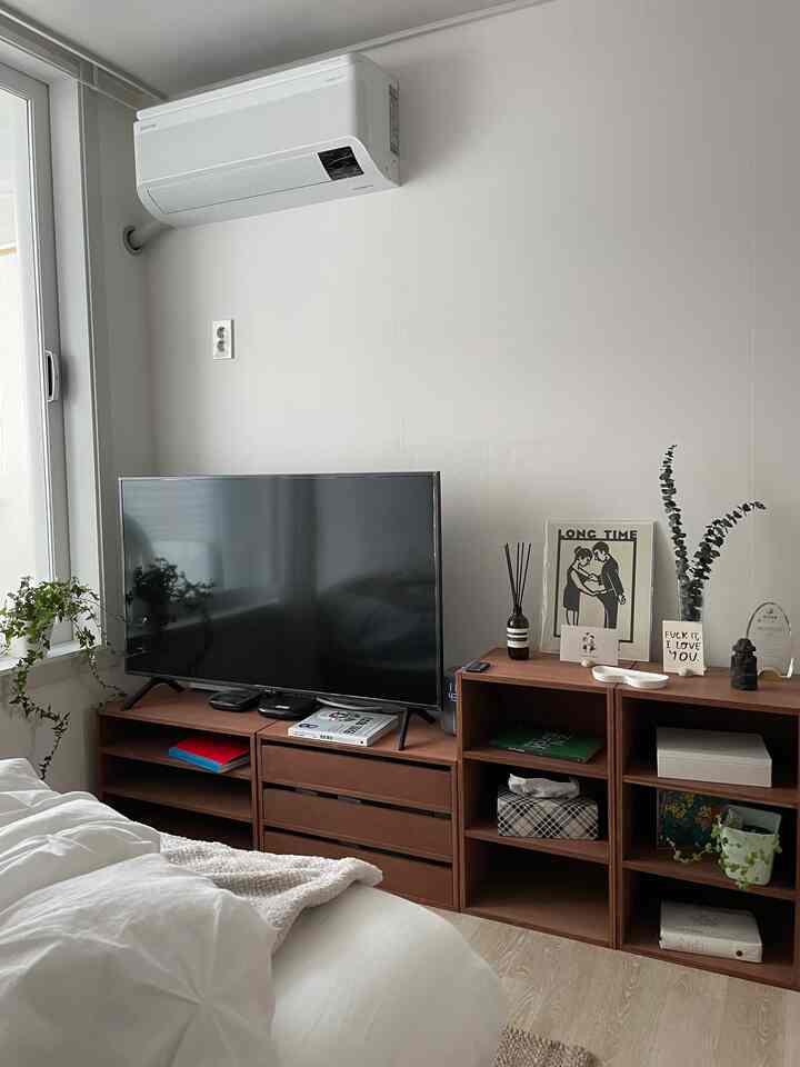 A modern bedroom with white walls and brown wooden furniture featuring a TV stand and bed as focal elements