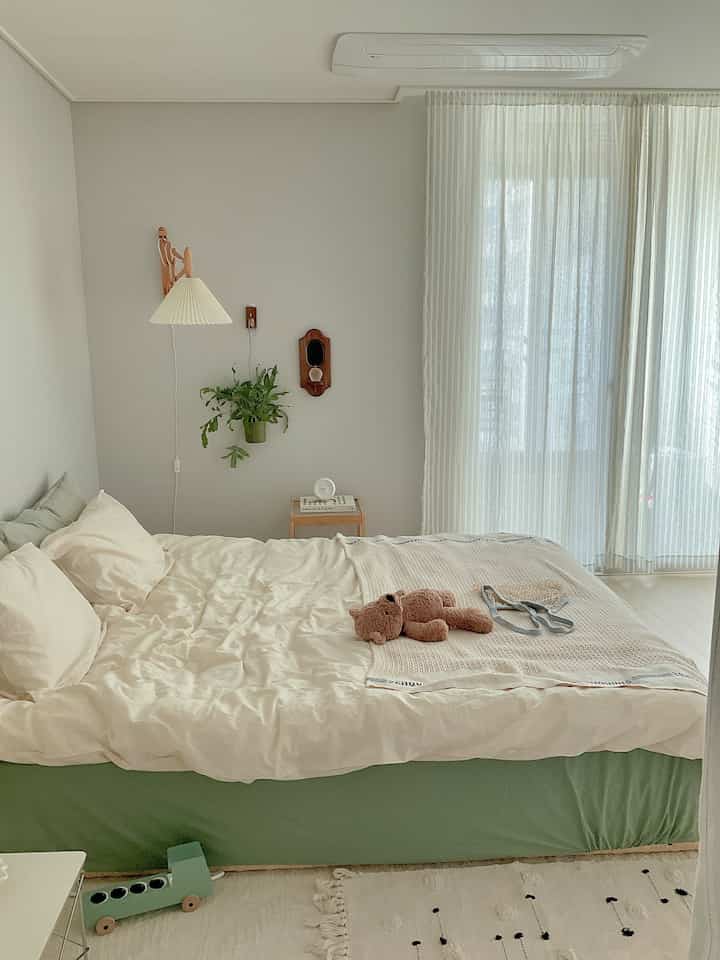 白と緑の色調の寝室、木製のナイトテーブルとテディベアが配置された雰囲気のあるインテリア