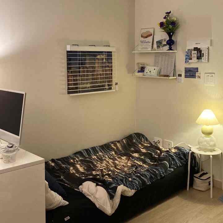 Cozy beige and white tone studio bedroom featuring blue star-patterned bedding and a table lamp creating warm ambiance