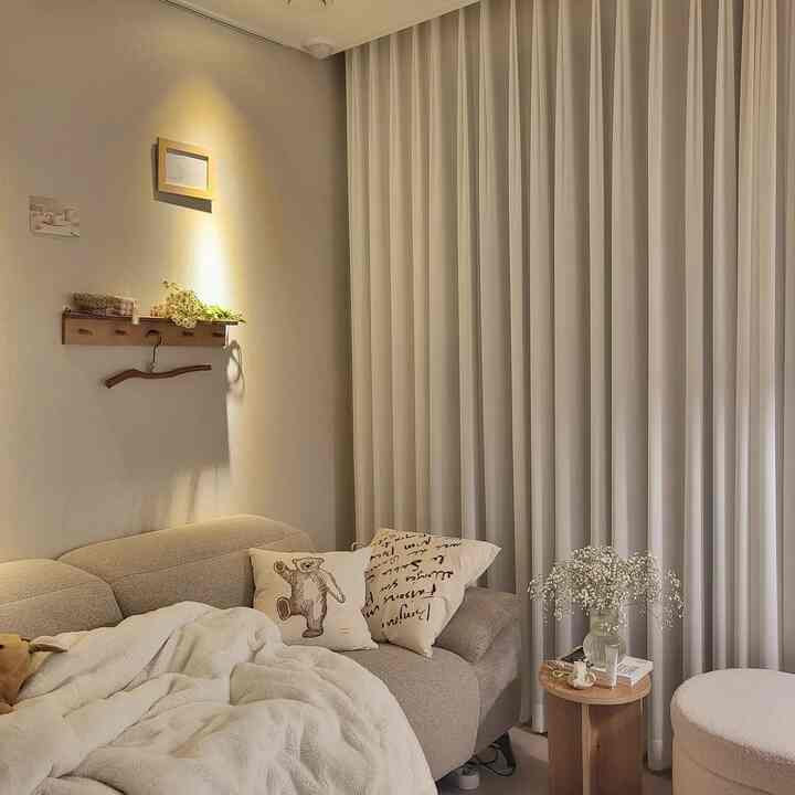 ベージュとホワイトの色調のリビング、ベージュのソファと白いカーテンが配置された落ち着いた空間