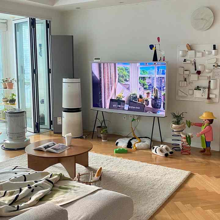 White and brown toned living room featuring a sofa, round coffee table, TV on a stand, and various plants creating a warm, cozy atmosphere
