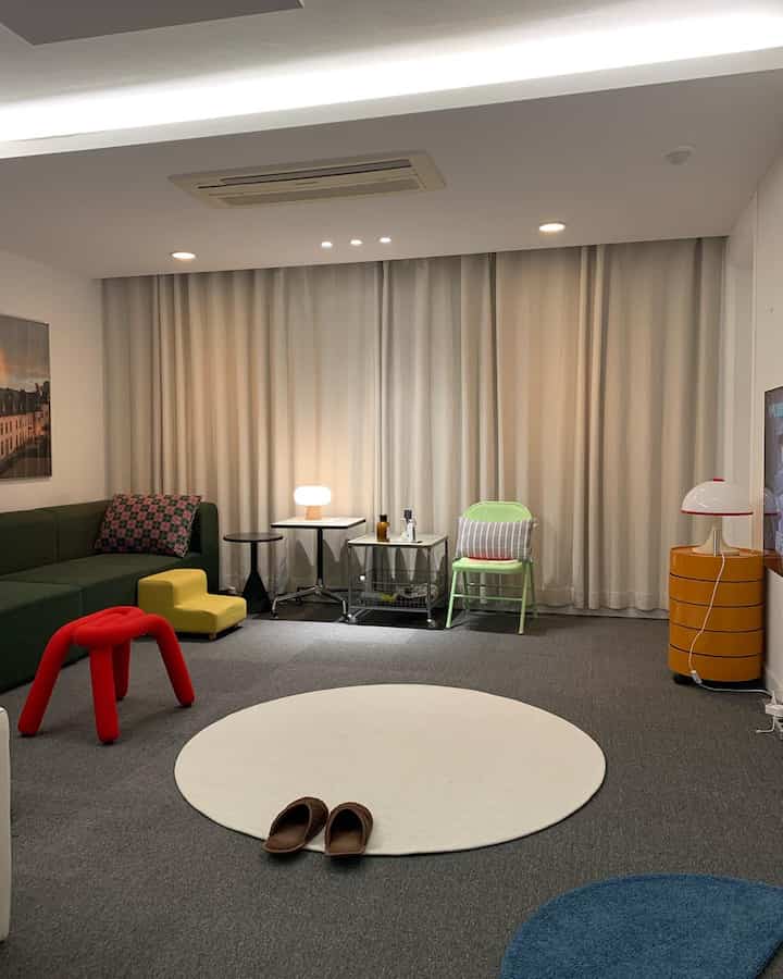 Beige-toned living room featuring a round rug, various stools, and blackout curtains creating a clean and cozy atmosphere