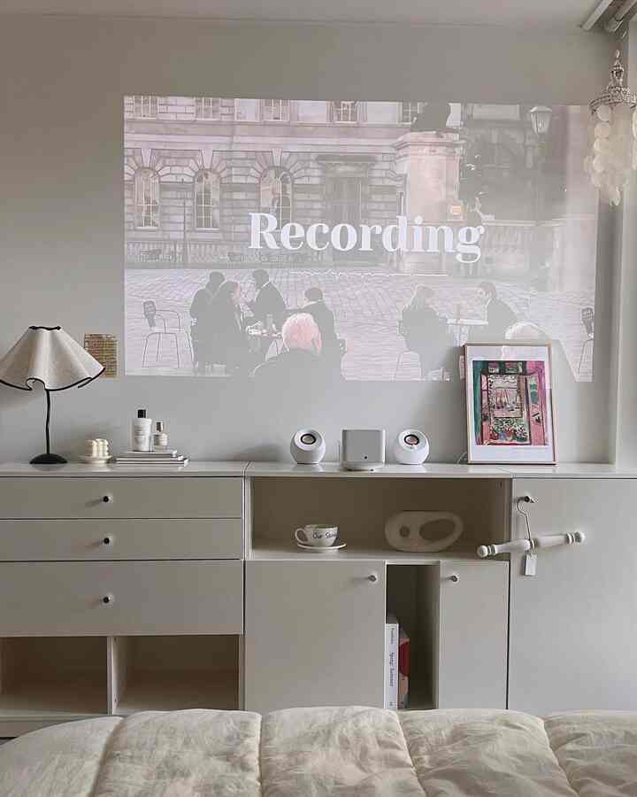 White-toned living room featuring projector screen and minimal storage units, creating a neat home cinema space