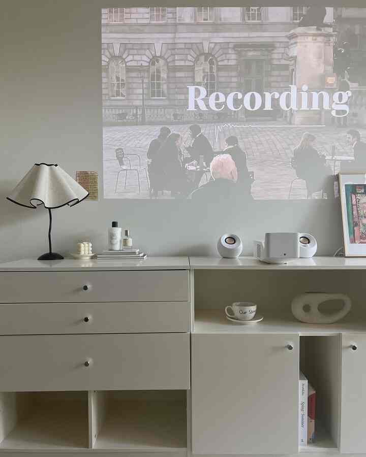 White-toned living room featuring a dresser, projector screen, and a unique table lamp in a clean modern interior