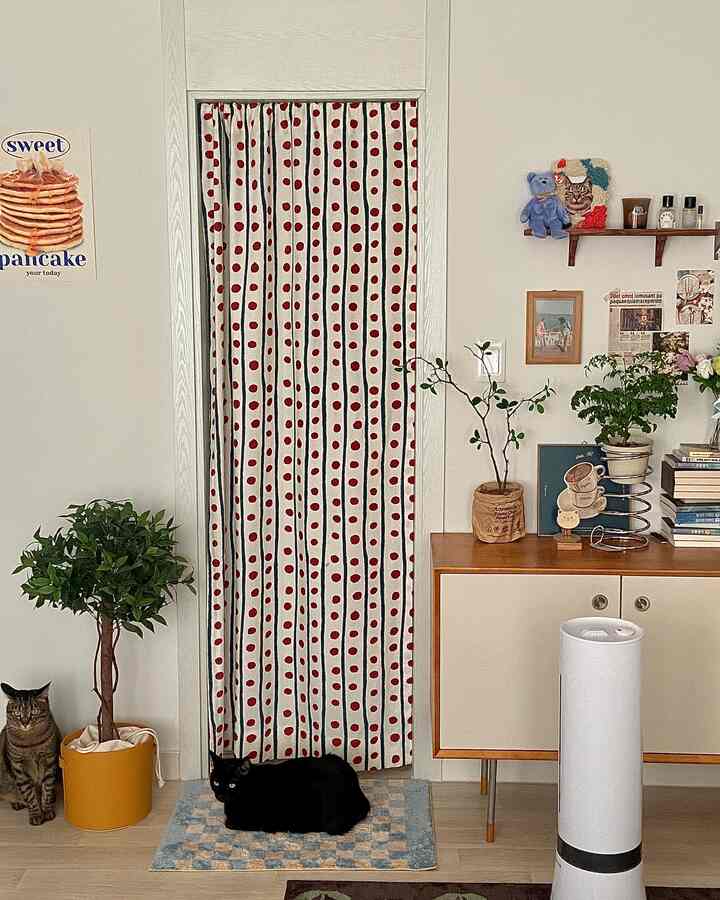 Beige-toned living room with red polka-dot curtain, featuring two cats and wood-tone cabinet creating cozy ambiance