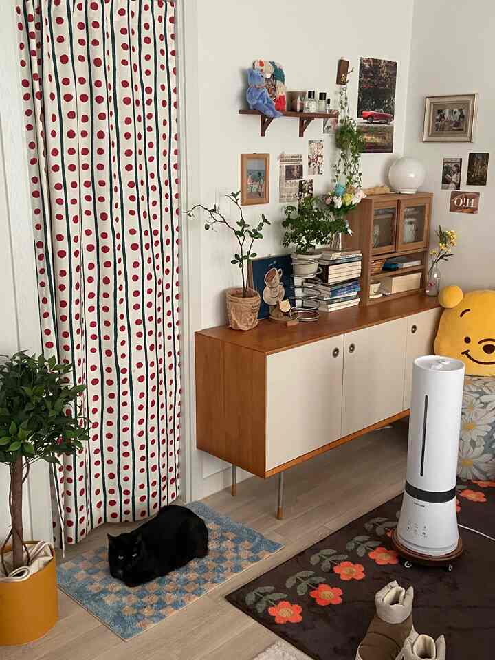 Natural toned living room with a black cat, featuring red polka dot curtains and a wooden sideboard creating a cozy atmosphere