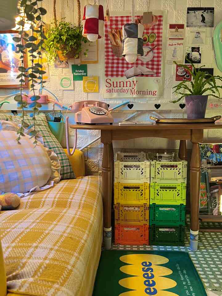 黄色のトーンの小さなリビング、レトロな電話やカラフルな収納箱、植物と温かみのある壁飾りが調和したインテリア