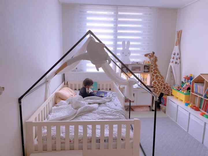 White-toned kids' room featuring a baby crib, toys, and bookshelves in a cozy play and sleep space