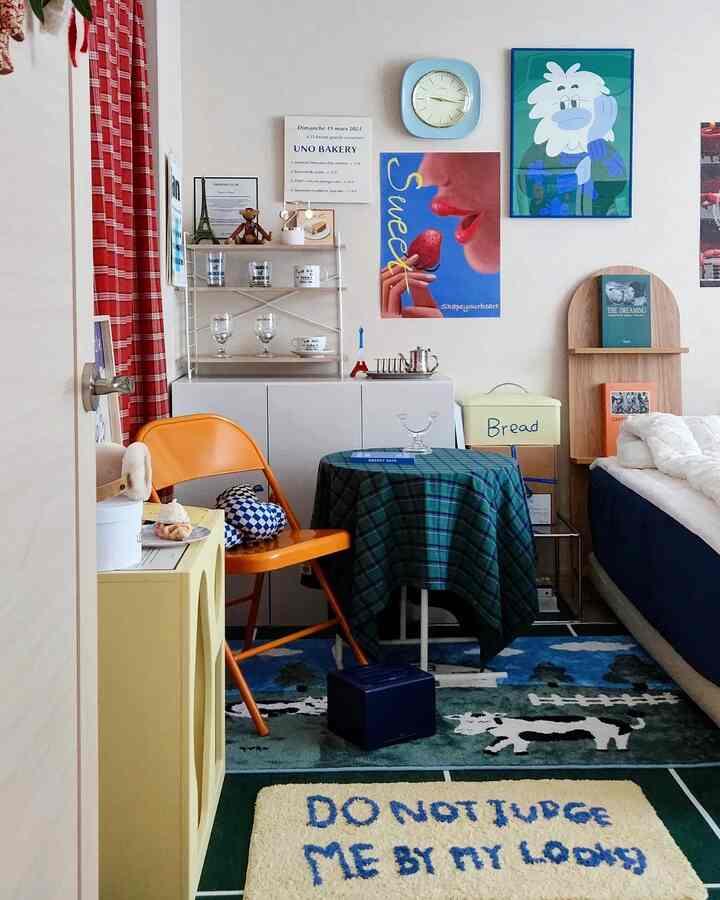 ネイビーと木目調が調和したコンパクトな寝室空間、オレンジの折りたたみ椅子とチェック柄テーブルクロスがアクセントの居心地の良いインテリア
