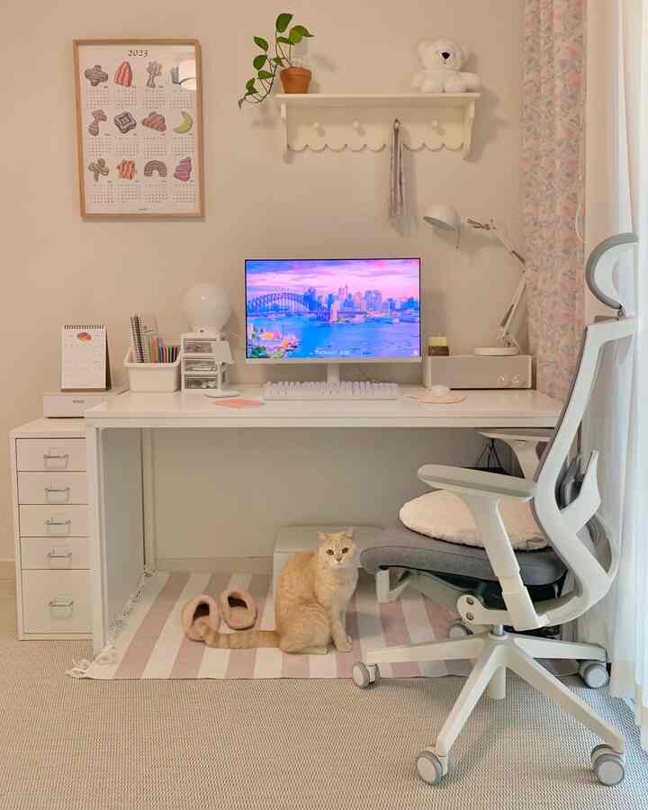 白とピンクのトーンのホームオフィス、きれいな机にコンピューターがあり、机の下にオレンジの猫が座る、温かみのある雰囲気のあるインテリア