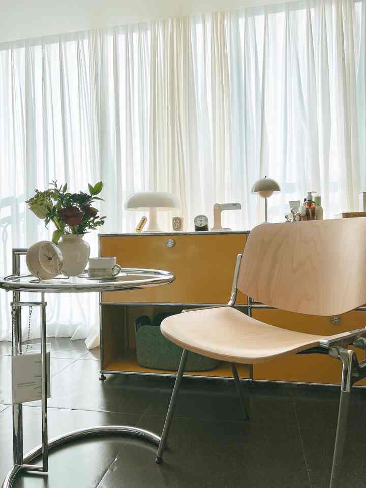 白と黄色のトーンのリビングコーナー、ナチュラルな木製椅子とクロームのサイドテーブルが配置されたモダンで自然な雰囲気のインテリア