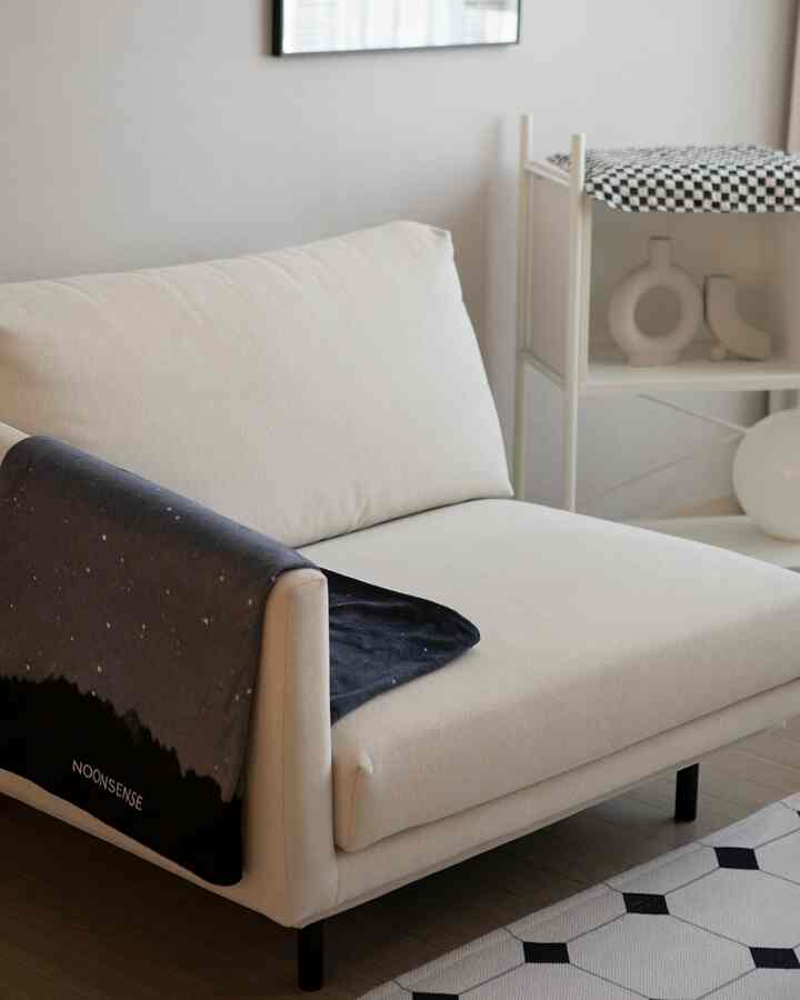 ベージュのモジュールファブリックソファと黒いブランケットが置かれたシンプルなリビングインテリア