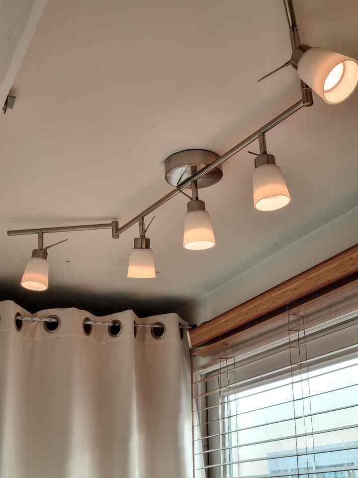 Modern space with white blackout curtains and wood tone blinds, featuring five-light ceiling track lighting that creates a warm atmosphere