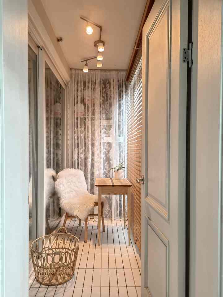 Bright wood tone and white long narrow balcony space featuring a small wooden table and a furry covered chair with a natural interior vibe