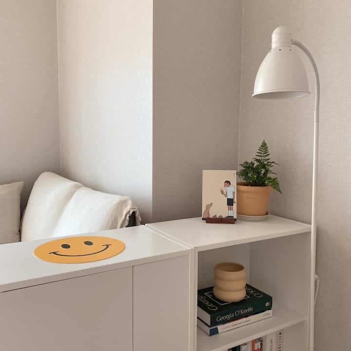White-toned study space featuring a two-seat sofa, bookshelf, floor lamp, and plant creating a clean and cozy atmosphere
