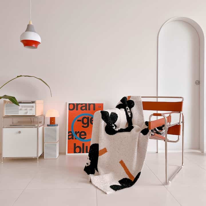 Bright white-toned modern living room featuring an orange-accented leather armchair draped with a patterned throw, and a pendant light creating a cozy atmosphere