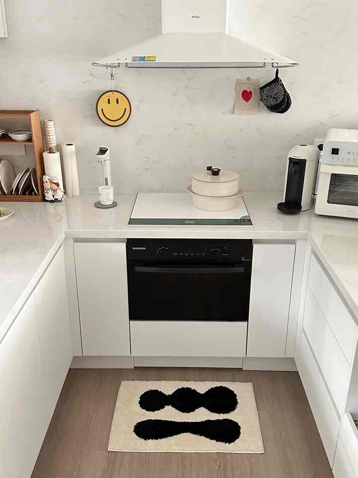 白と木目調が調和したモダンで清潔感のあるキッチン、中央に黒い模様のフロアマットとビルトイン調理器具が配置された印象的な空間