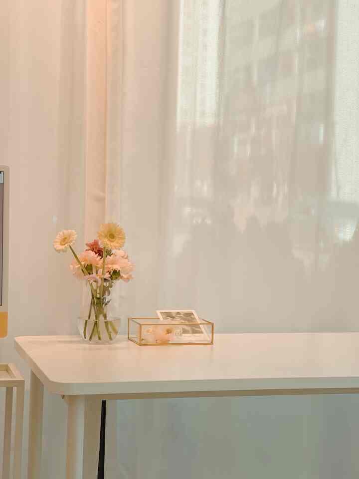White and beige toned home office featuring a simple desk with a vase and photo frame, a quiet workspace atmosphere