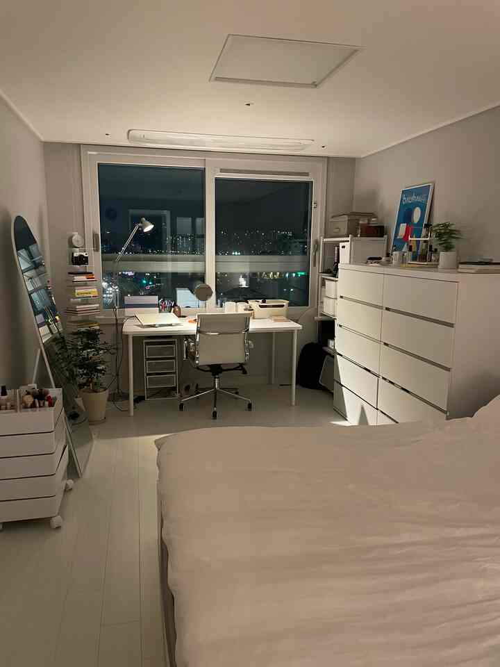 白を基調とした寝室兼ホームオフィス空間、大きな窓とデスク、椅子、チェストが配置されたミッドセンチュリーモダン風の雰囲気あるインテリア