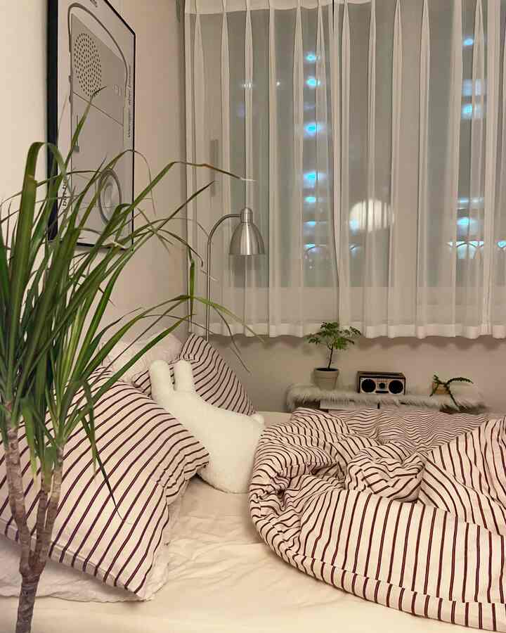 White and burgundy striped bedroom featuring curtains, a floor lamp, and plants in a cozy setting