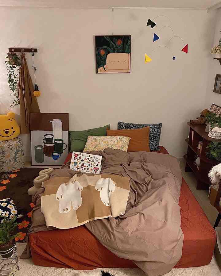 ベージュとブラウンの色調の寝室、中央に居心地の良いベッドと温かみのある掛け布団カバーがあり、壁にはアートと多彩な小物が配置された雰囲気のあるインテリア