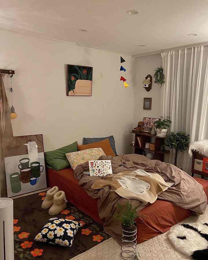 Brown and white toned single bedroom featuring a cozy bed with pillows and cushions, decorated with plants creating a natural atmosphere