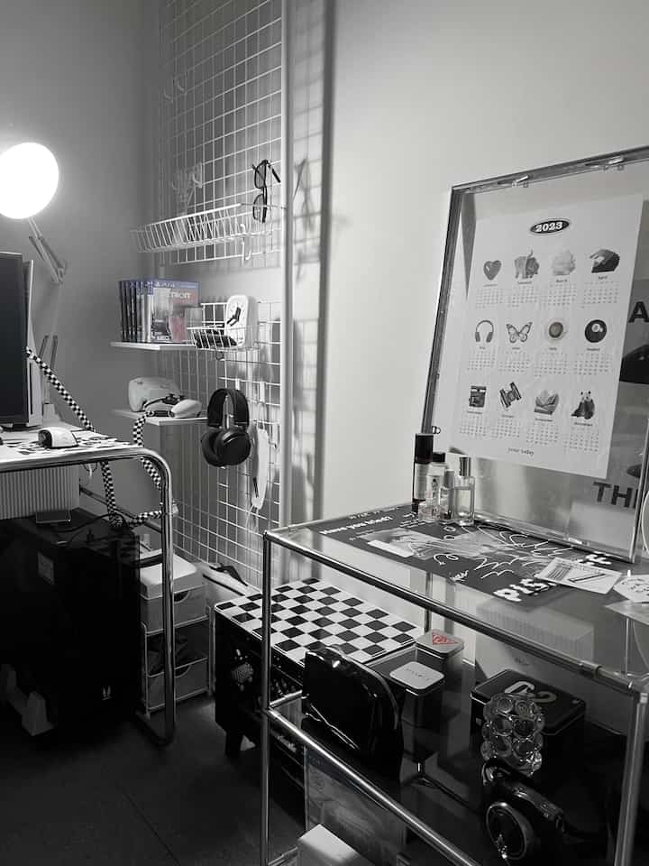 Monotone white and black home office space featuring a desk and metal shelves neatly holding gaming devices and accessories