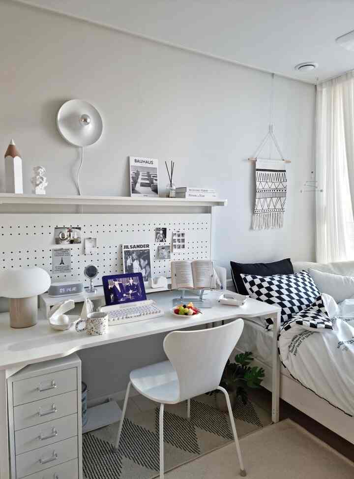 白を基調とした寝室兼ホームオフィス、シンプルなデスクと装飾品が配置された落ち着いた印象のインテリア