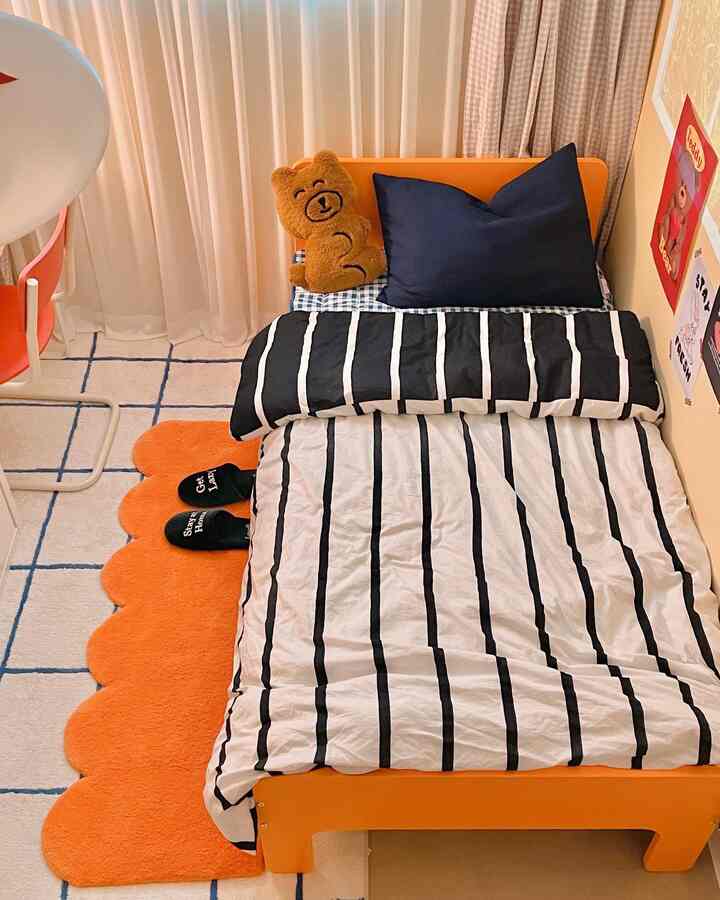 Orange and navy toned kids' bedroom featuring a cute teddy cushion, striped bedding, and wall posters in a cozy space