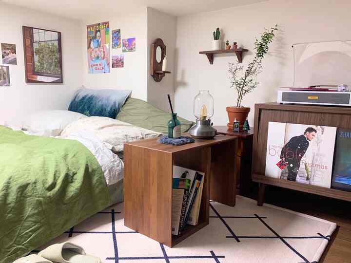Natural wood-tone studio bedroom featuring green bedding and plants creating a cozy atmosphere
