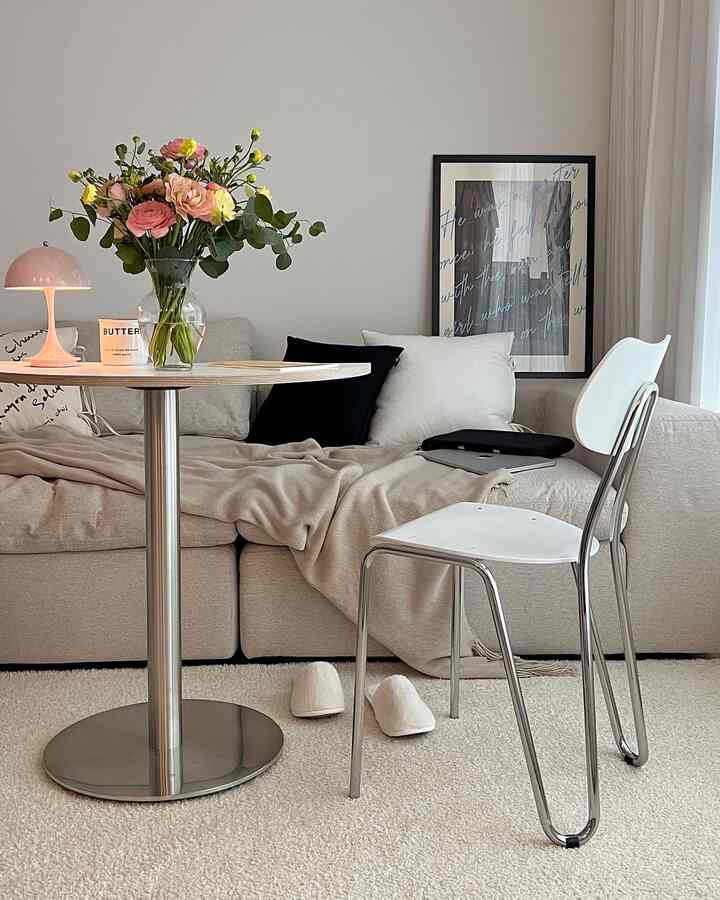 Bright beige and white toned living room featuring a sofa, round table, vase with flowers, and table lamp in a natural modern style