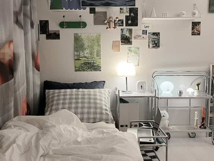 A white and gray-toned bedroom featuring a bed with checkered pillow centrally, metal nightstand with lamp on the right in a minimal Scandinavian style space