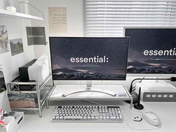 A modern home office in white and gray tones featuring dual monitors on a monitor stand neatly arranged on a clean desk