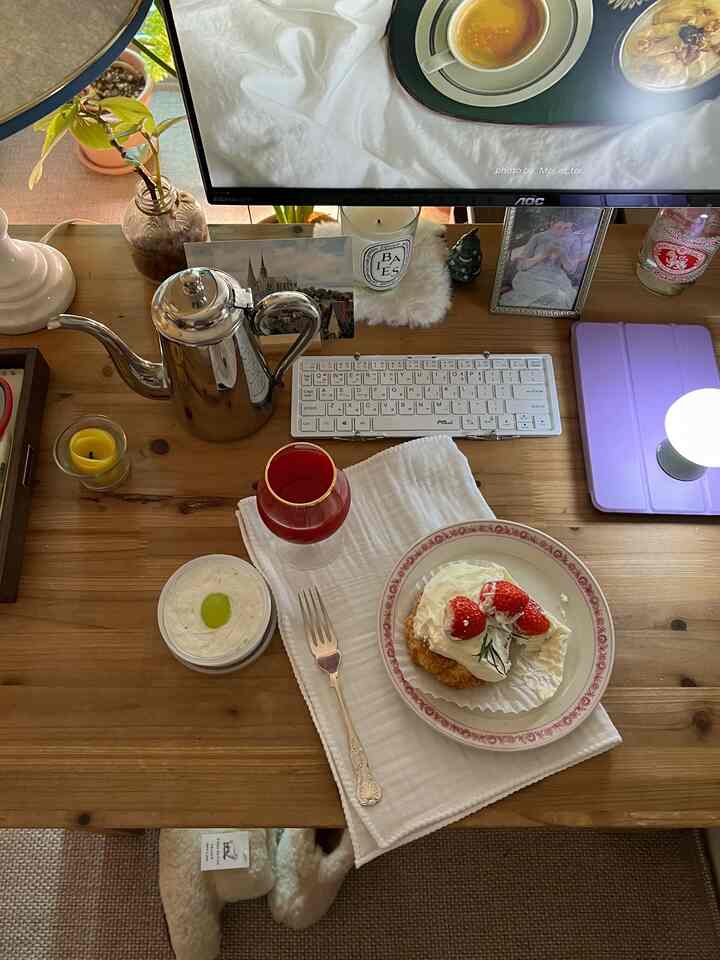 Cozy home office space on warm wood table featuring keyboard, cutlery, cake, and candles arranged neatly