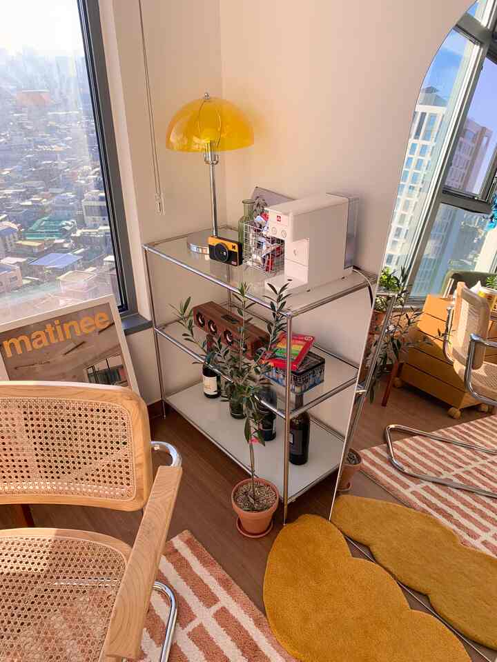 White and yellow toned living room featuring metal shelving, wooden armchair, and a coffee machine in a natural modern style