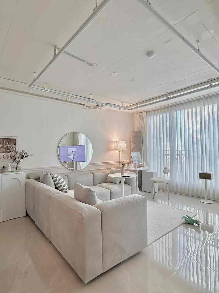 白を基調としたリビング、広いソファとラグ、丸い鏡とフロアランプが配置されたモダンですっきりとしたインテリア