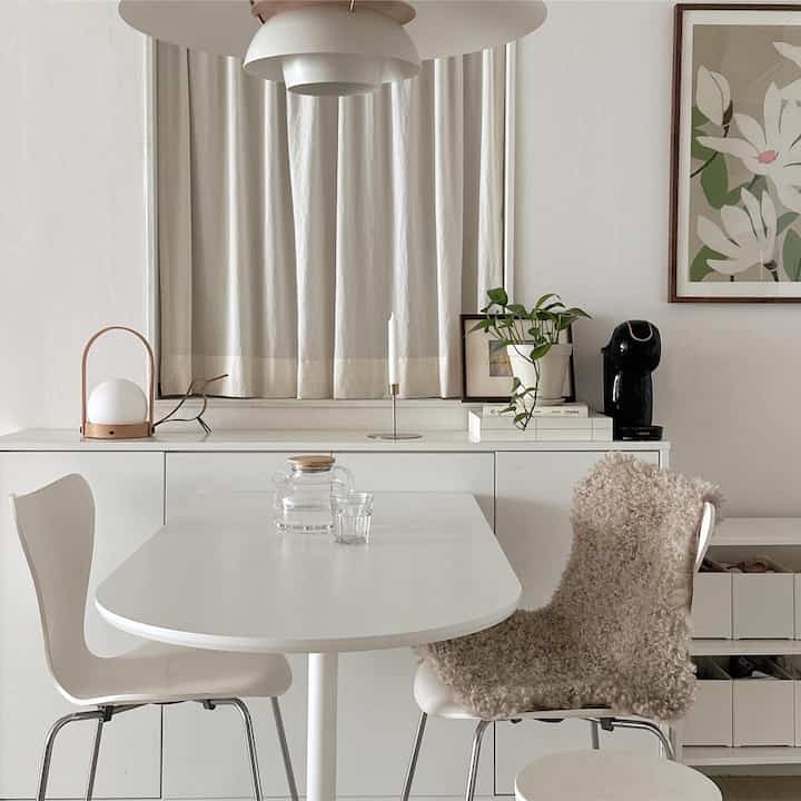 White-toned dining room featuring a simple dining table and chairs, coffee machine and plant creating a neat and cozy atmosphere