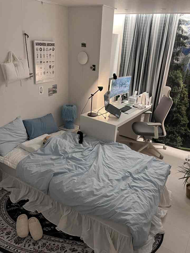 White-toned studio bedroom with blue bedding featuring a compact workspace and home office setup