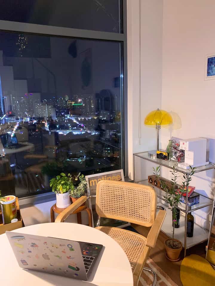White and wood-tone studio apartment featuring a round table, armchair, and yellow lamp creating a cozy home office ambiance