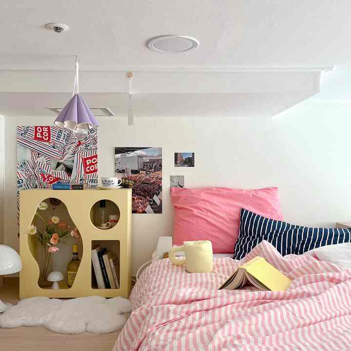 柔らかなピンクとバターイエローの調和があるロフト寝室、ミニマルな収納キャビネットと居心地の良い寝具が配置された空間