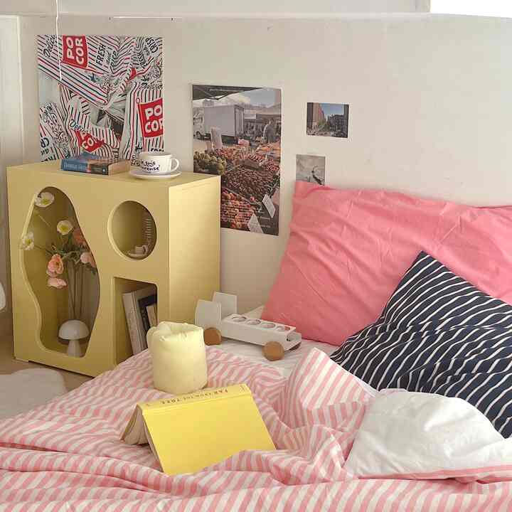ピンクと黄色の色調が映える寝室、ミニマルな家具と個性的な収納キャビネットが配置された雰囲気のあるインテリア