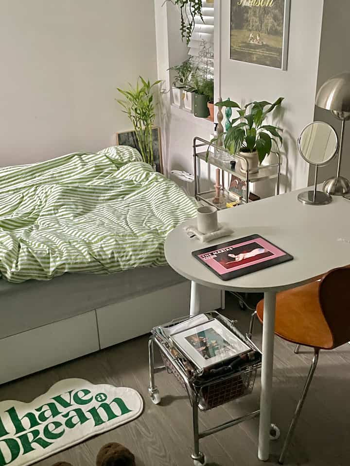 White and green toned bedroom featuring a bed, desk, and various plants creating a cozy atmosphere