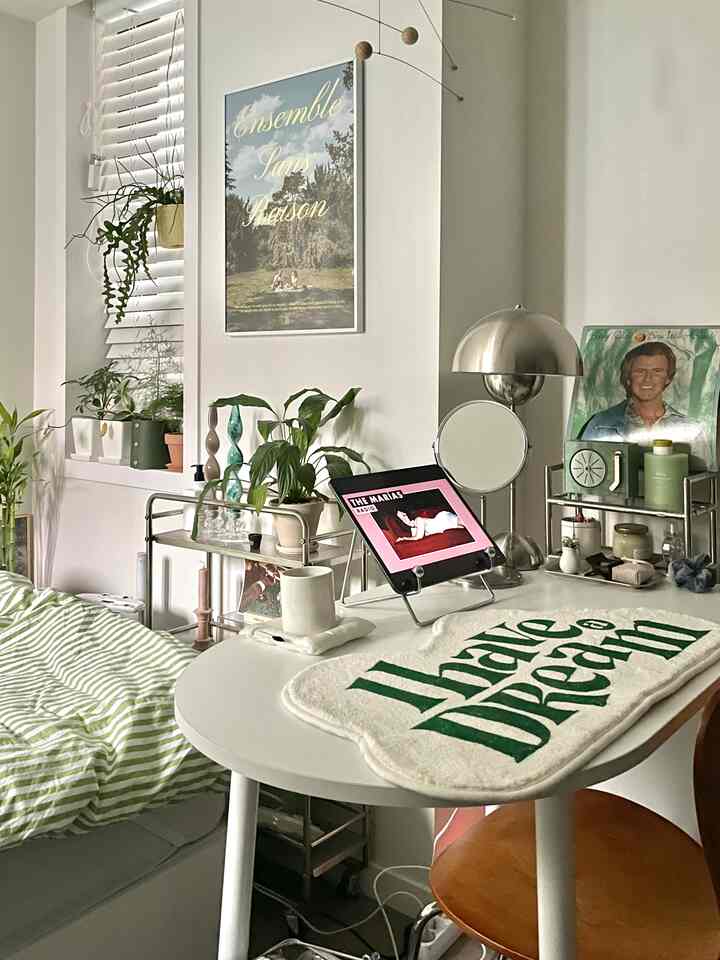 Small room in white and natural tones featuring a desk, wooden stool, and various plants, cozy single household space