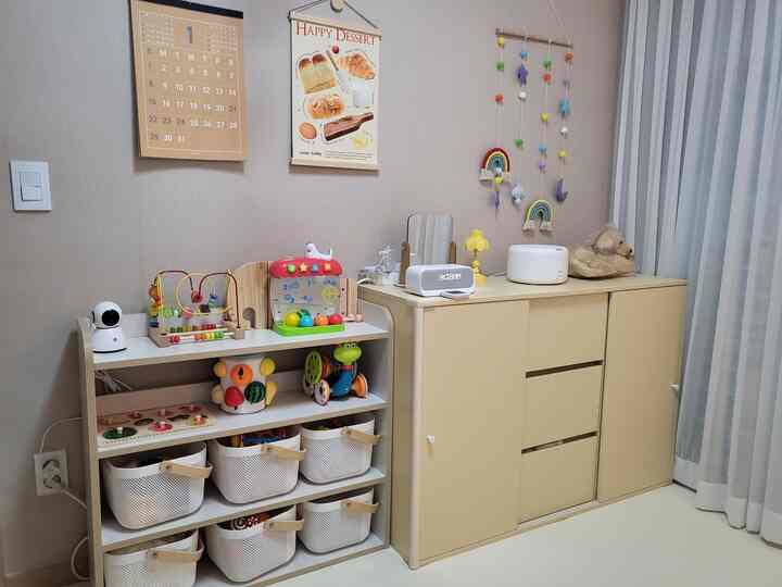 ベージュと白の色調の子供部屋、玩具収納棚と壁飾りが配置された落ち着いた整頓されたインテリア