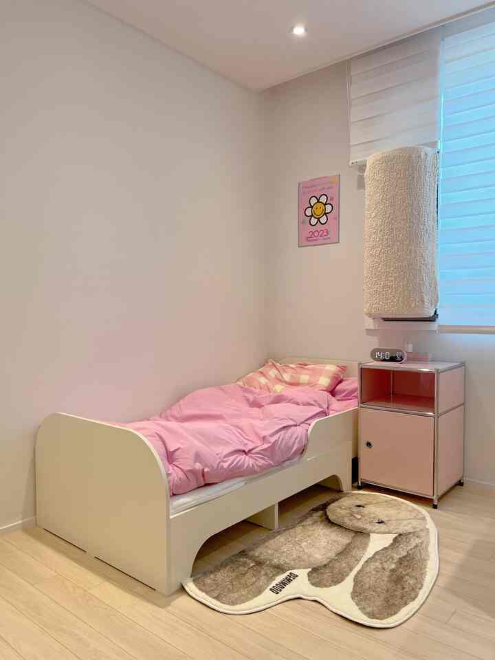 白とピンクを基調とした子供部屋、シングルベッドとピンクのナイトテーブル、ウサギ形のラグが配置された温かみのあるインテリア