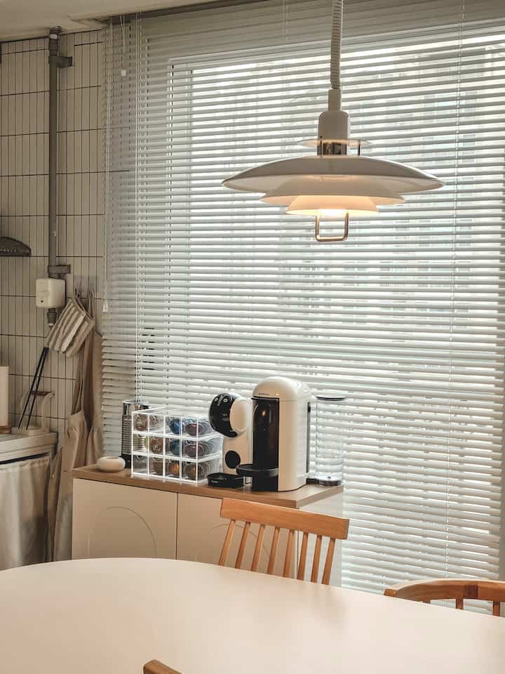 白と木目調が調和したキッチン空間、ダイニングテーブルとシンプルなペンダントライトが配置された清潔感のあるおうちカフェのインテリア