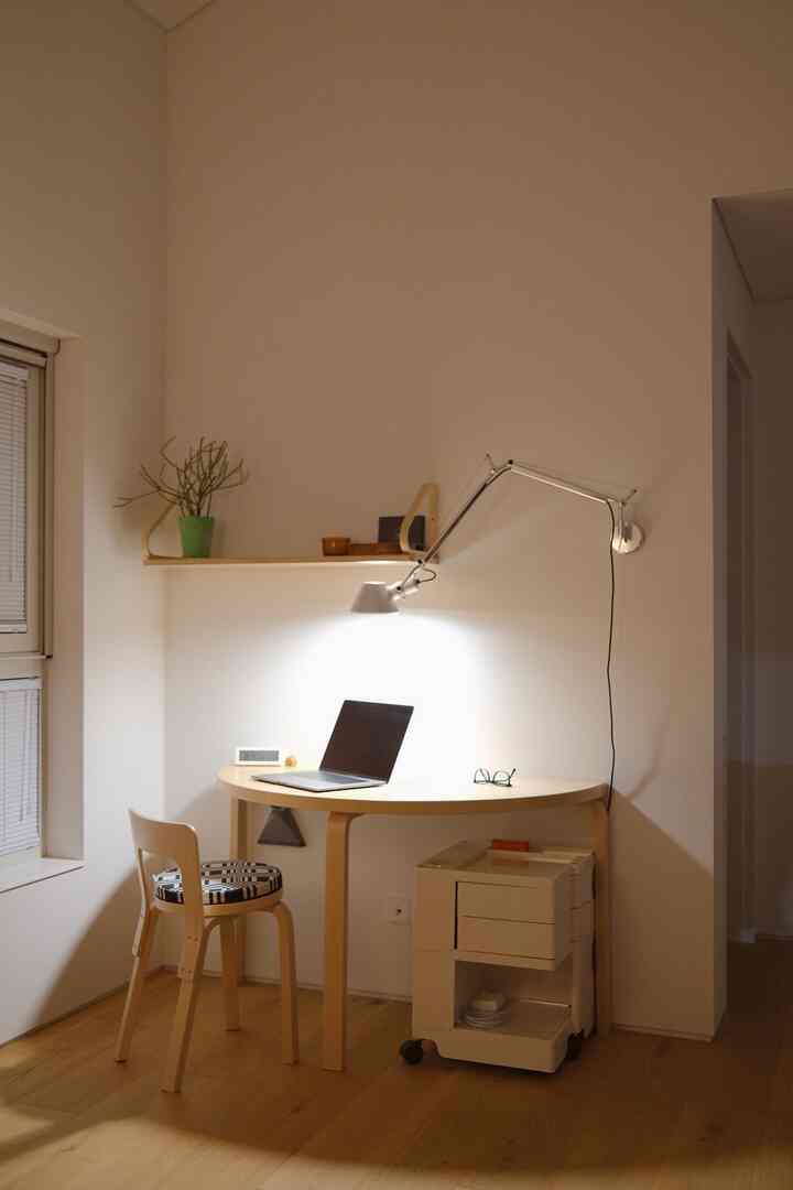 暖かい木目調と白い壁のコンパクトな書斎、半円形の机と椅子、壁掛けランプが配されたミニマルな作業空間