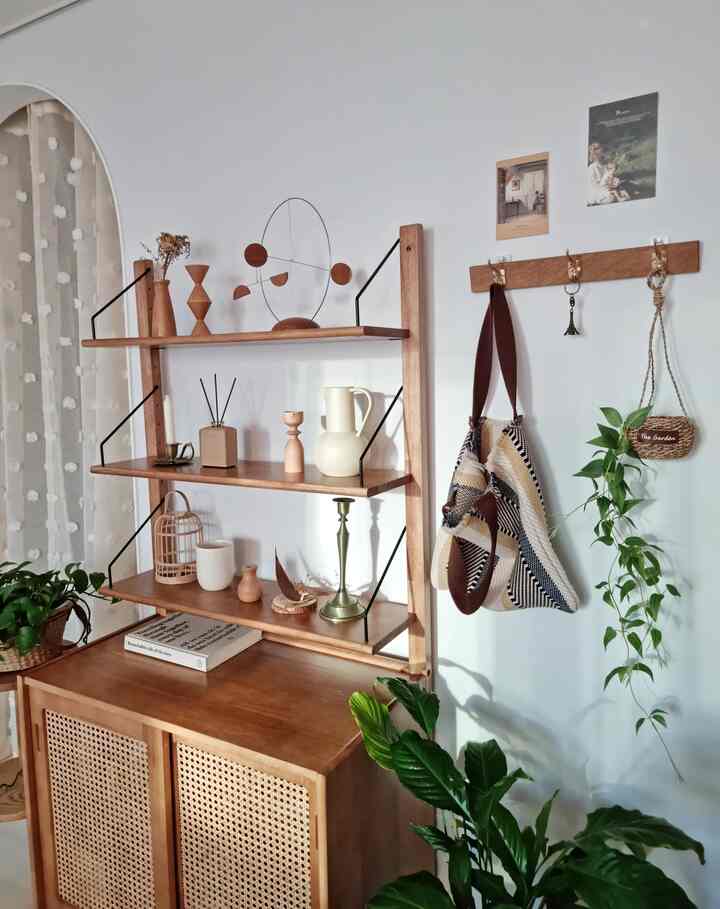 Natural tone room featuring wood-tone cabinet, shelves with objets, coat rack, and green plants creating a cozy atmosphere