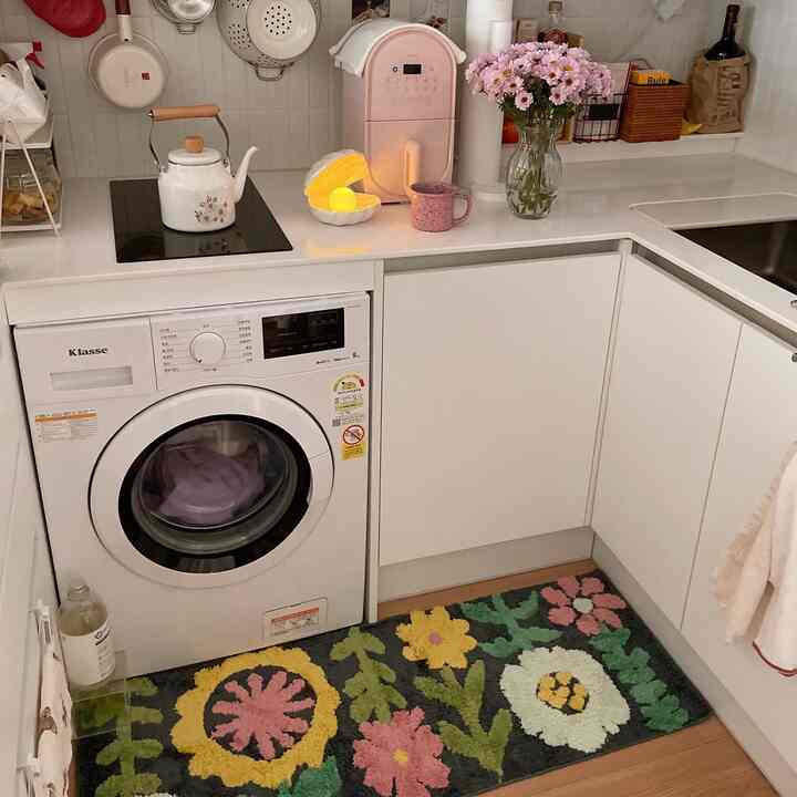 明るいホワイトトーンのキッチン、モダンな家電と花柄のバスマットが配置された雰囲気のある空間